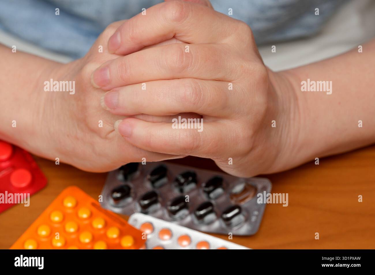 Una persona siede su un tavolo di legno, le mani unite, riflettendo un pensiero profondo. Foto Stock