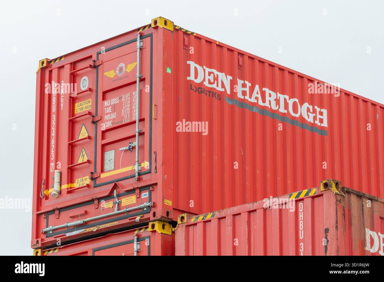 Contenitori di spedizione rossi dalla logistica di den hartogh impilati contro un cielo limpido Foto Stock