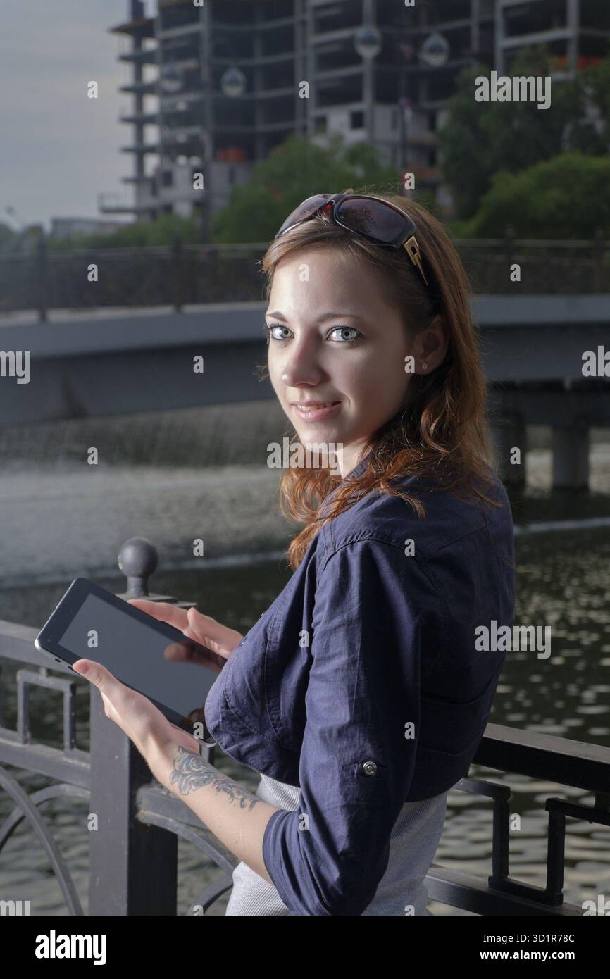 Le donne d'affari di Redhead con un computer tablet guardano indietro contro l'edificio in via di sviluppo Foto Stock