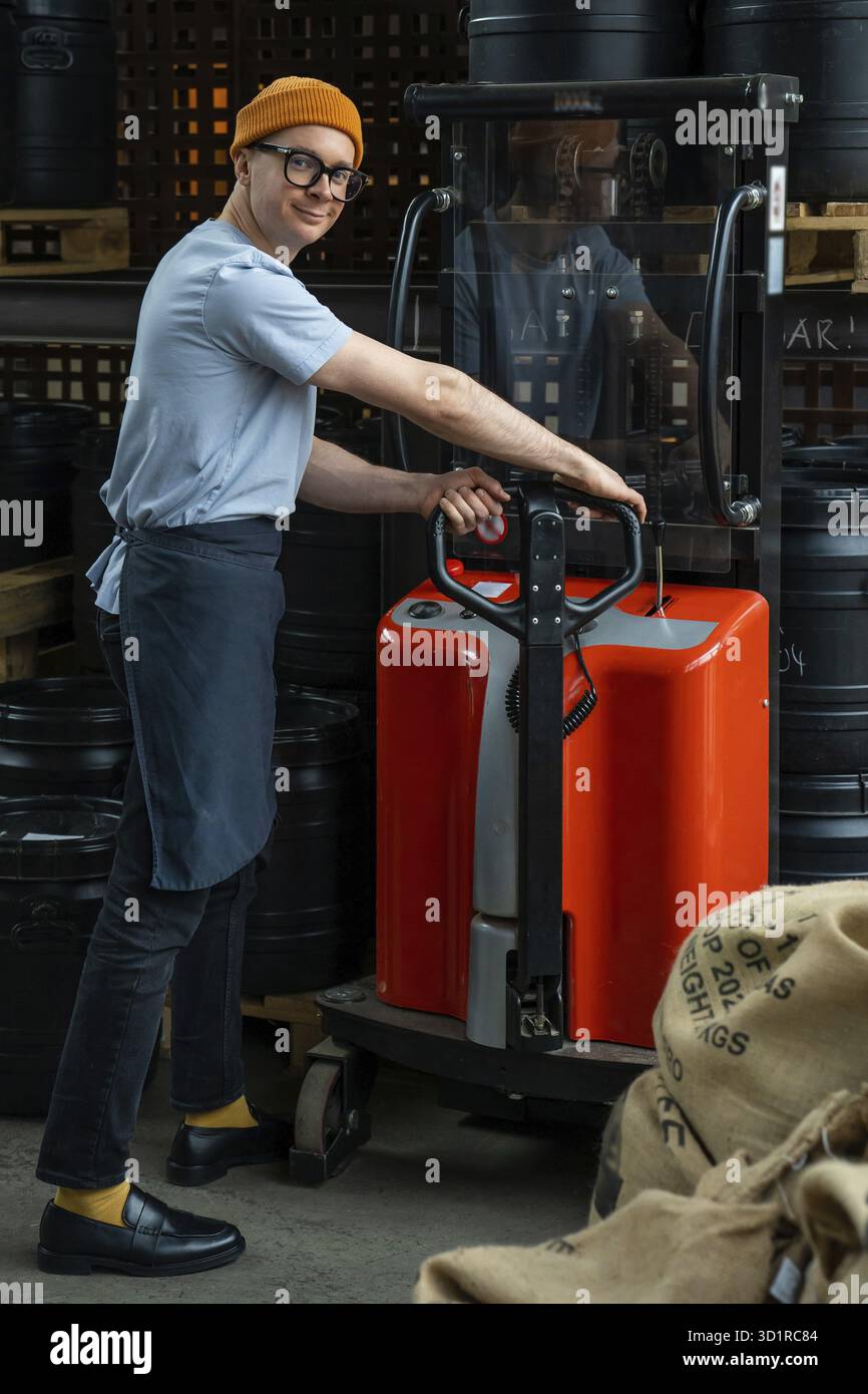 Uomo hipster con cappello e grembiule che tostera il lavoratore della fabbrica che prepara i chicchi di caffè per la preparazione del caffè Foto Stock
