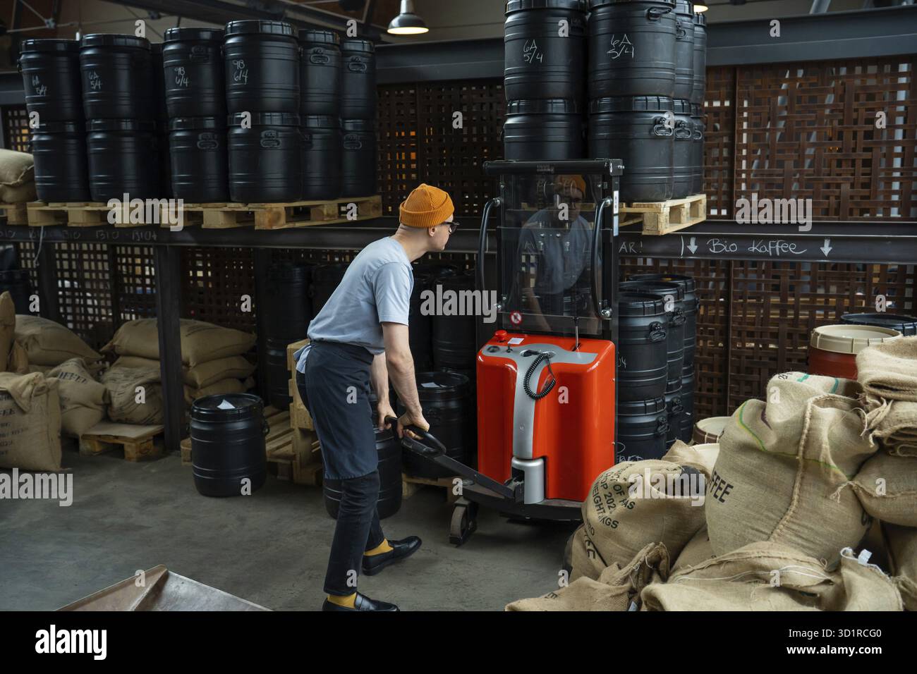 Uomo hipster con cappello e grembiule che tostera il lavoratore della fabbrica che prepara i chicchi di caffè per la preparazione del caffè Foto Stock