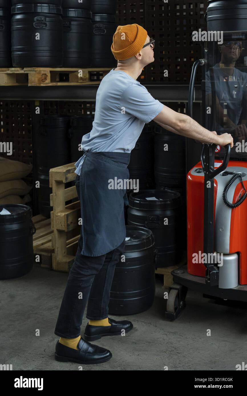 Uomo hipster con cappello e grembiule che tostera il lavoratore della fabbrica che prepara i chicchi di caffè per la preparazione del caffè Foto Stock