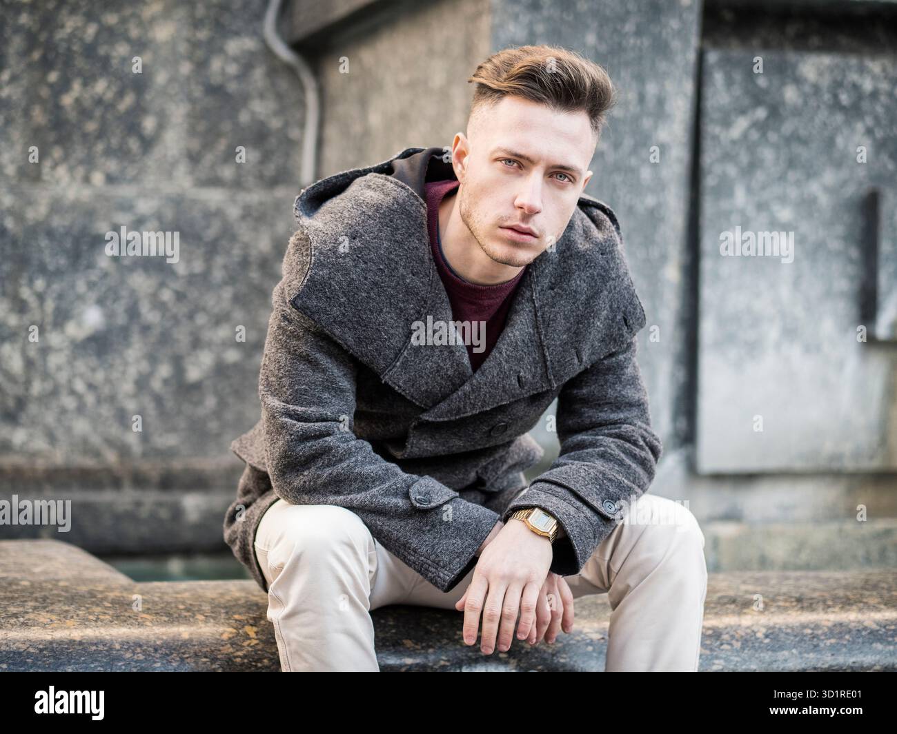 Giovane uomo seduto presso la fontana, guardando la macchina fotografica in città impostazione Foto Stock