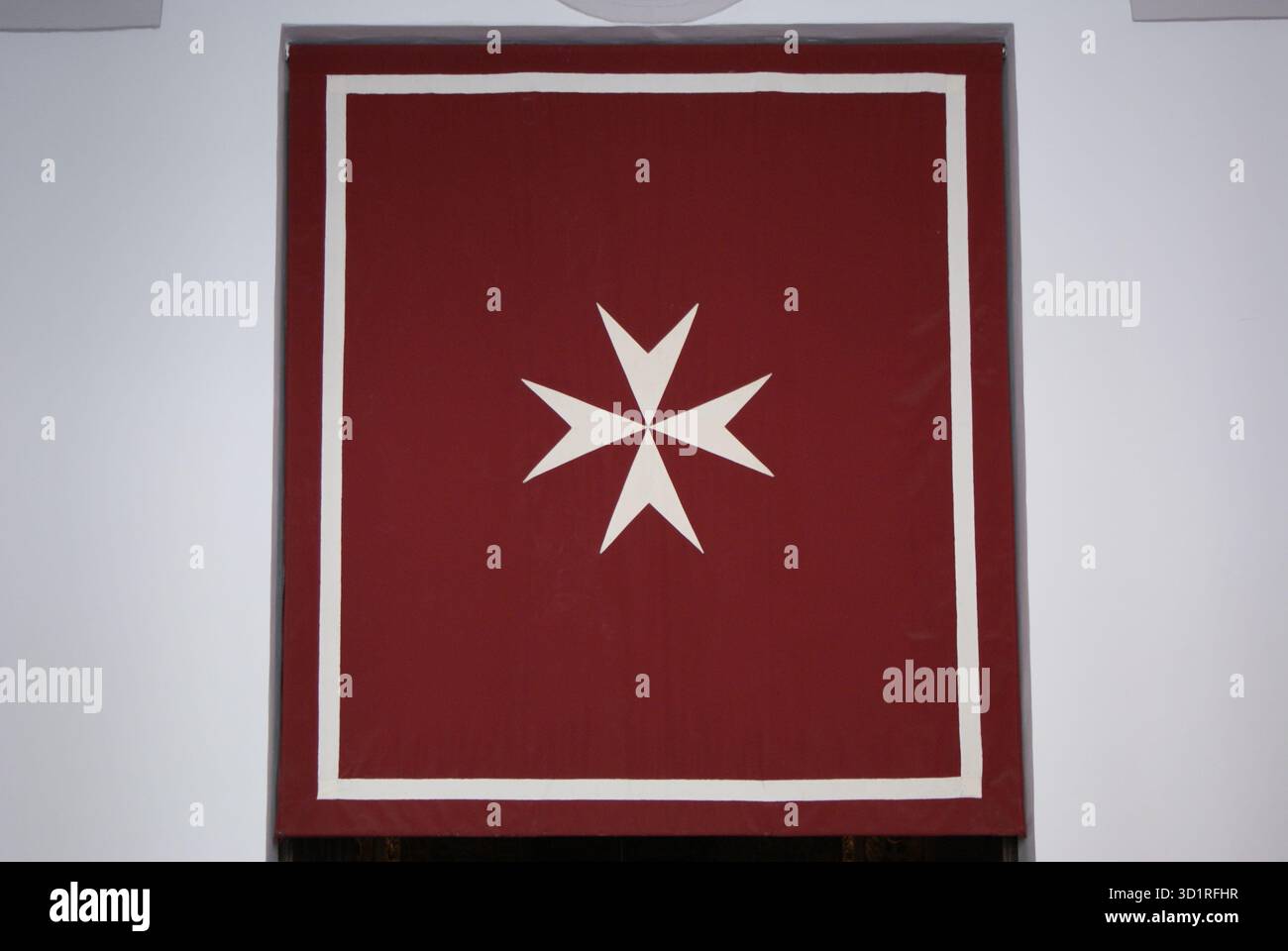 Simbolo della croce maltese presentato su uno stendardo rosso con un bordo bianco, che rappresenta concetti storici o spirituali Foto Stock