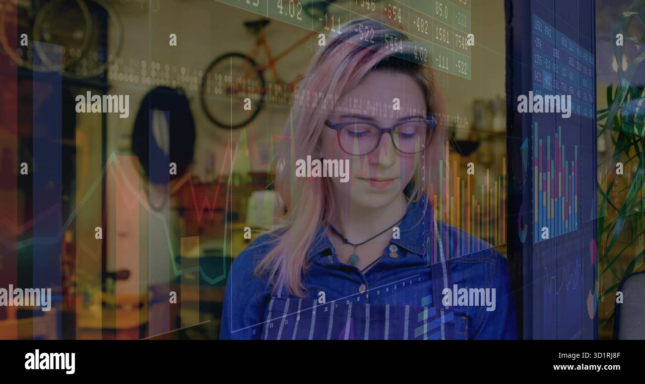 Donna che indossa un grembiule a righe che crea in officina ed esamina la sovrapposizione digitale vicino alla bicicletta montata Foto Stock