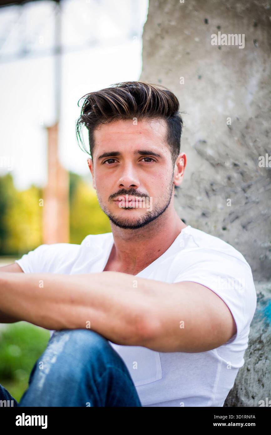 Bell'uomo giovane in una t-shirt bianca all'aperto in un ambiente urbano Foto Stock