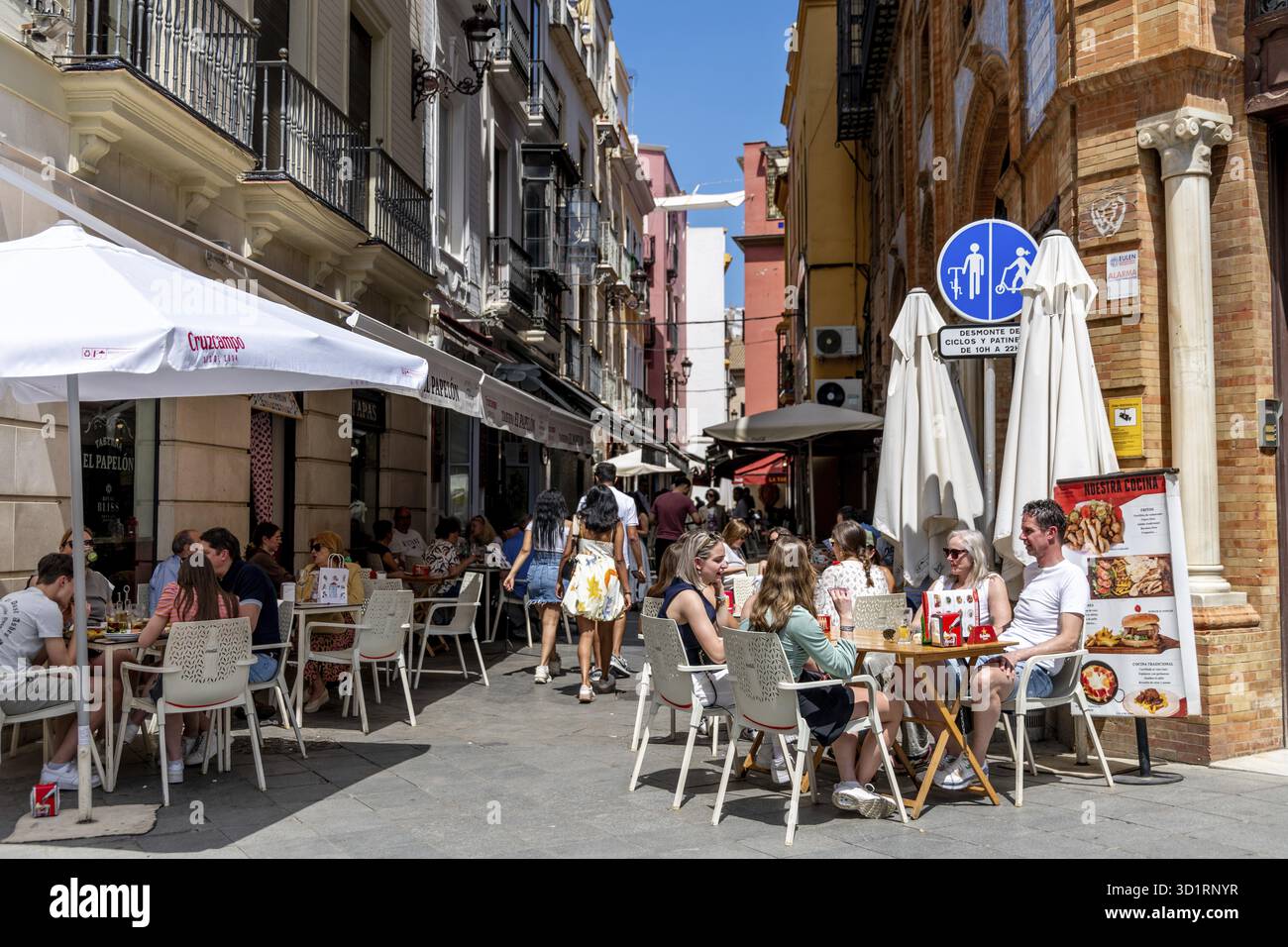 Siviglia, Siviglia - Spagna â€“ 04-19-2024: Una strada trafficata piena di caffè e ristoranti sul marciapiede dove i turisti e la gente del posto si siedono, bevono un caffè e Foto Stock