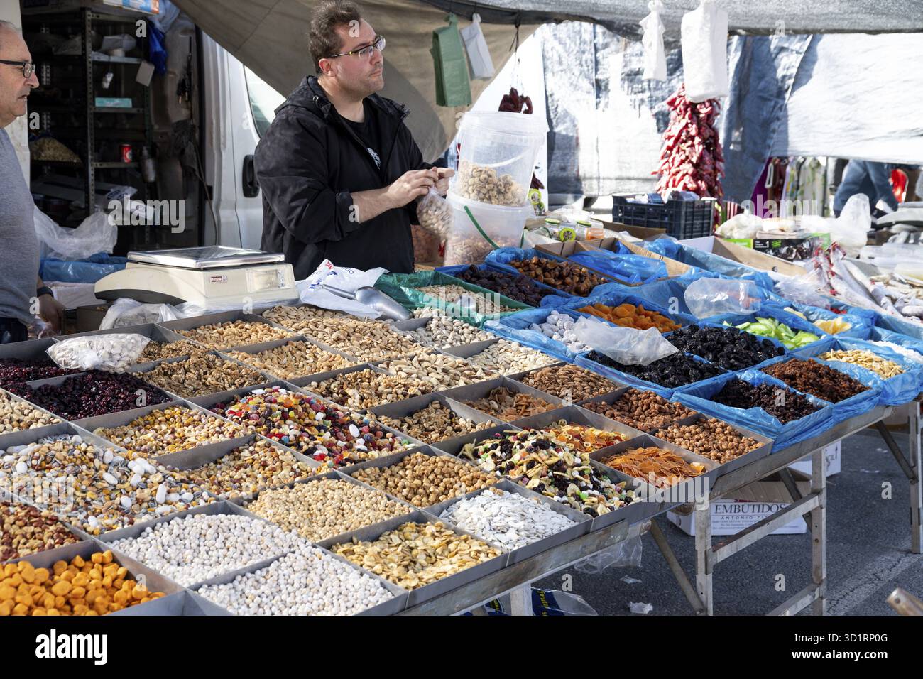 Guadix, Granada - Spagna - 01-24-2024: Uno stand di mercato con frutta secca, noci e semi in vari contenitori, mentre il venditore prepara le merci per la dogana Foto Stock