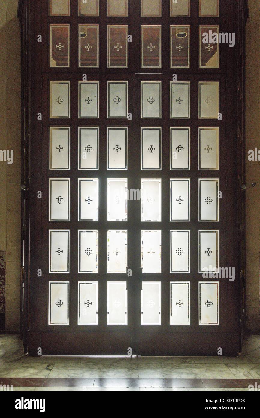 Catania, Sizilien - Italia - 04-15-2025: Porta in legno con pannelli in vetro smerigliato con motivi geometrici a croce, situata all'interno della Cattedrale di Foto Stock
