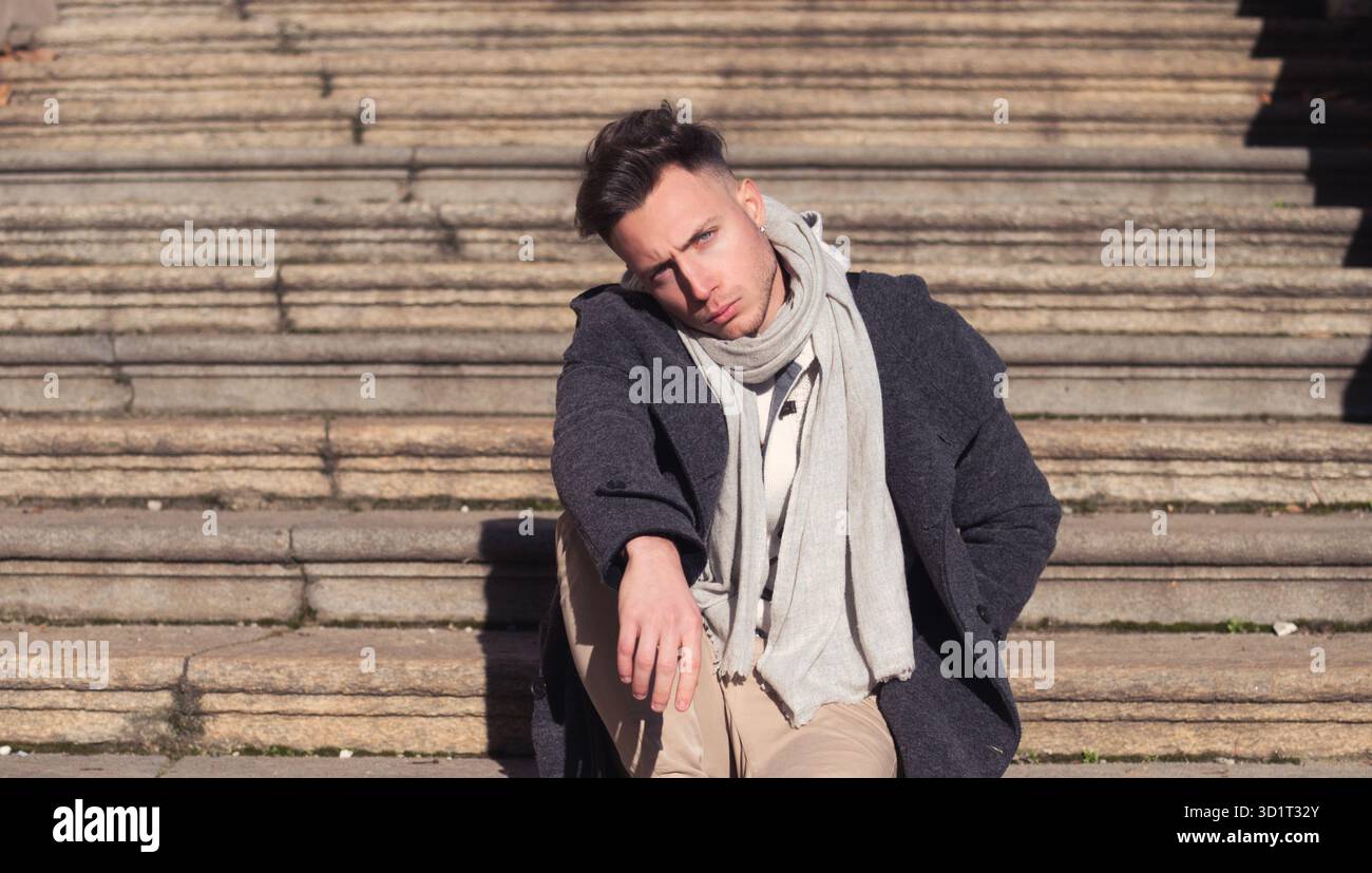 Bel giovane uomo all'aperto seduto su scale di pietra all'esterno Foto Stock