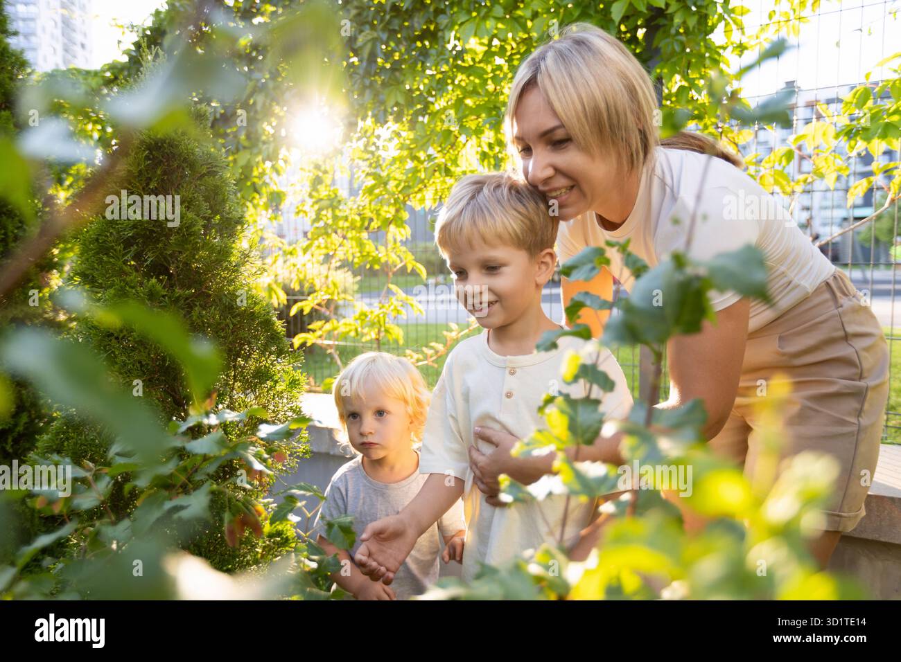 Mamma che si gode del tempo di qualità con i suoi due figli al parco giochi in un pomeriggio di sole Foto Stock