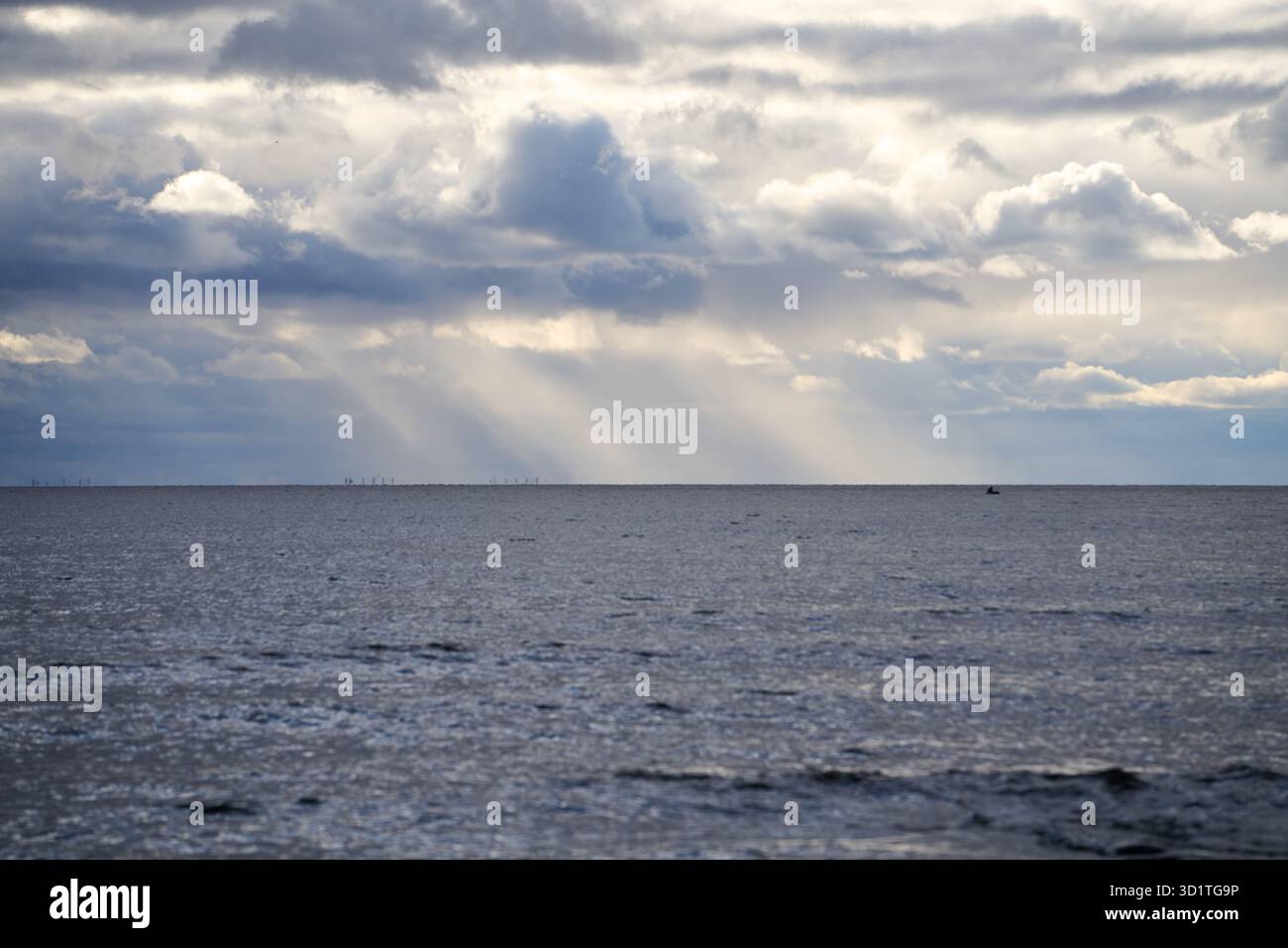 Vista sul mare dei tenui raggi del sole che piangono le dense nuvole sopra il mare calmo grigio-blu, catturata alla luce naturale dalla riva con linea all'orizzonte e atmosfera Foto Stock