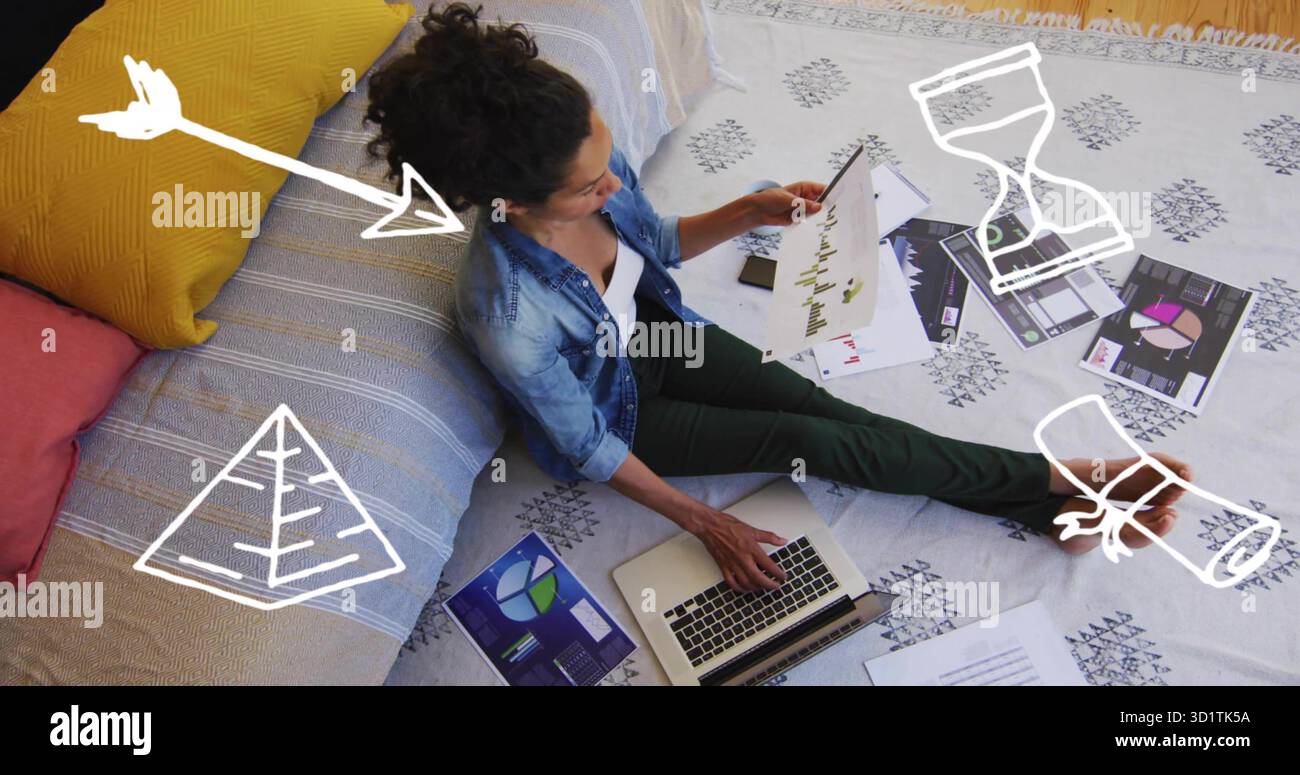 Donna che scrive sul laptop e che esamina carte stampate sul pavimento della camera da letto, con carta sparsi Foto Stock