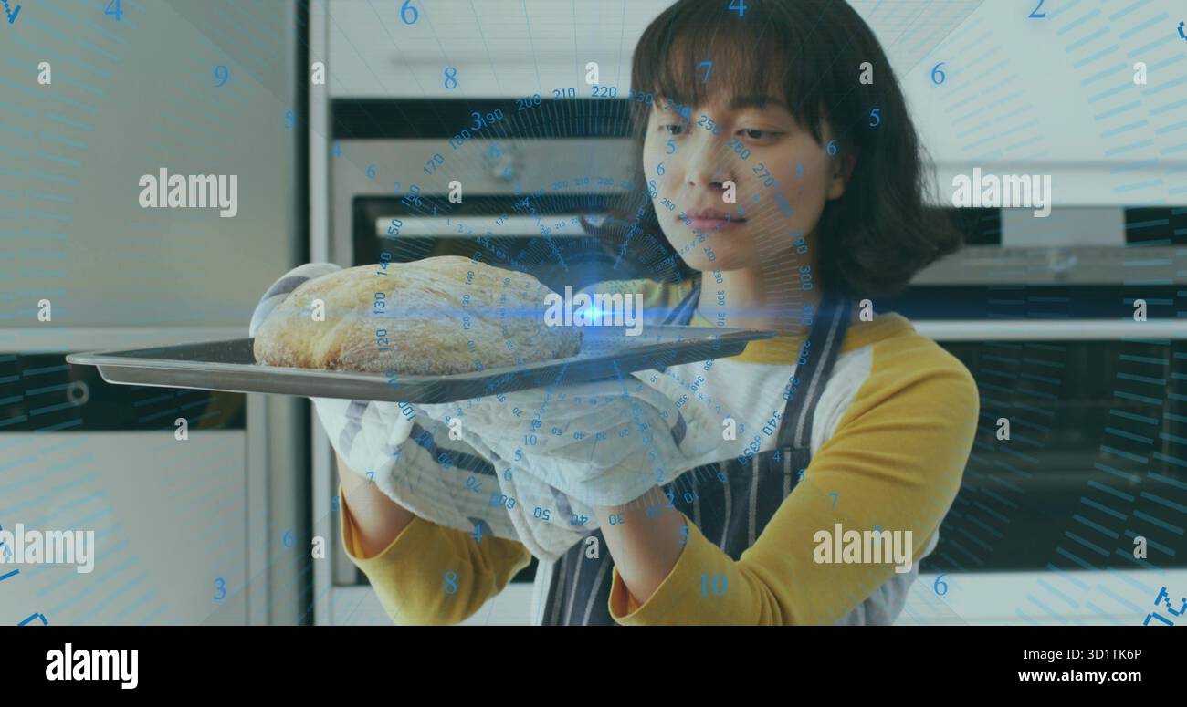 Donna asiatica che tiene vassoio con pane, indossa guanti da forno in cucina con forni, con griglia digitale Foto Stock
