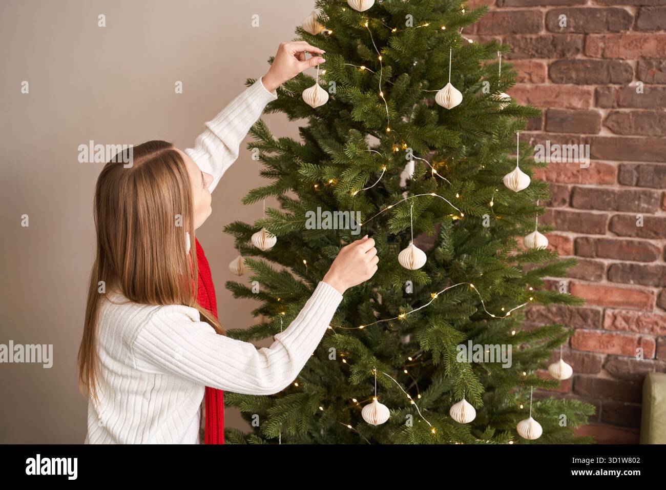 Una giovane donna veste l'albero di natale al chiuso. Ritratto delle vacanze in casa. Blogger Foto Stock
