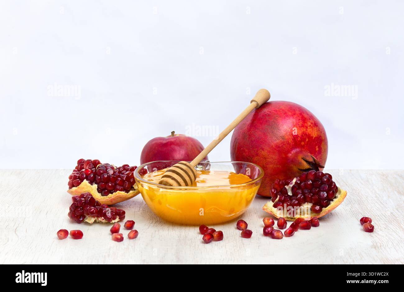 Miele nel recipiente di vetro, mele rosse, granati su un tavolo di legno bianco su sfondo chiaro con spazio per il testo Foto Stock