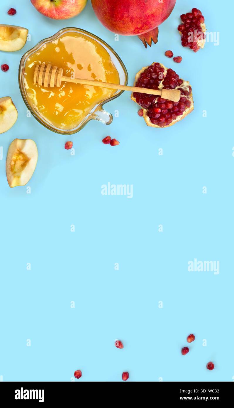Miele nel recipiente di vetro, mele rosse, granati, cucchiaia di miele di legno su sfondo blu con spazio per il testo. Vista dall'alto, disposizione piatta Foto Stock