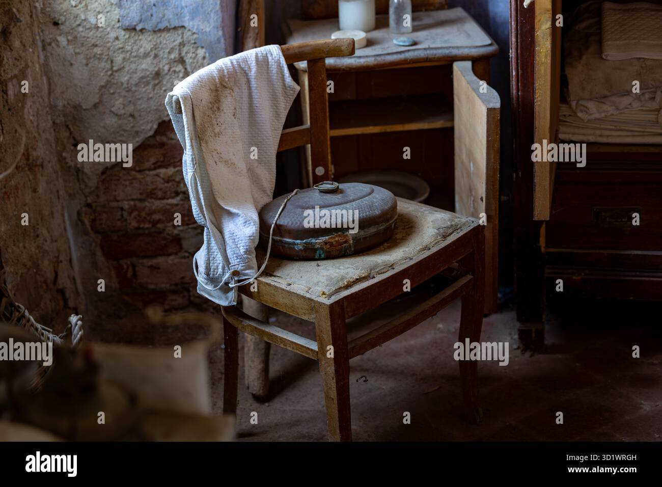 Scalda letto vintage in metallo su sedia in legno con interni rustici abbandonati Foto Stock