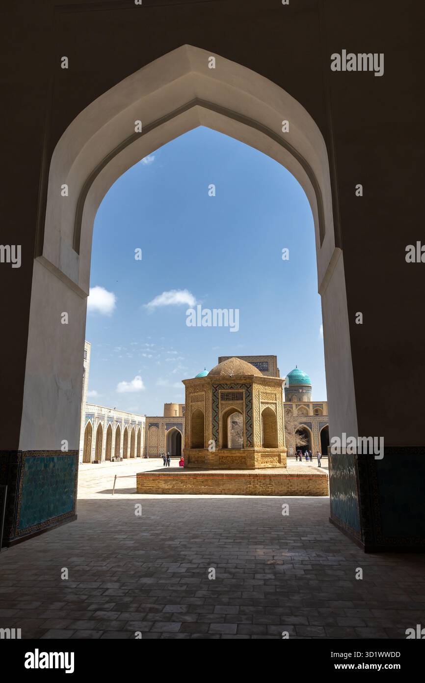 c - 27 marzo 2024: Un grande arco incornicia un cortile illuminato dal sole dominato da una storica moschea Kalyan, il complesso po-i-Kalyan. È accreditato allo sceicco Abdull Foto Stock