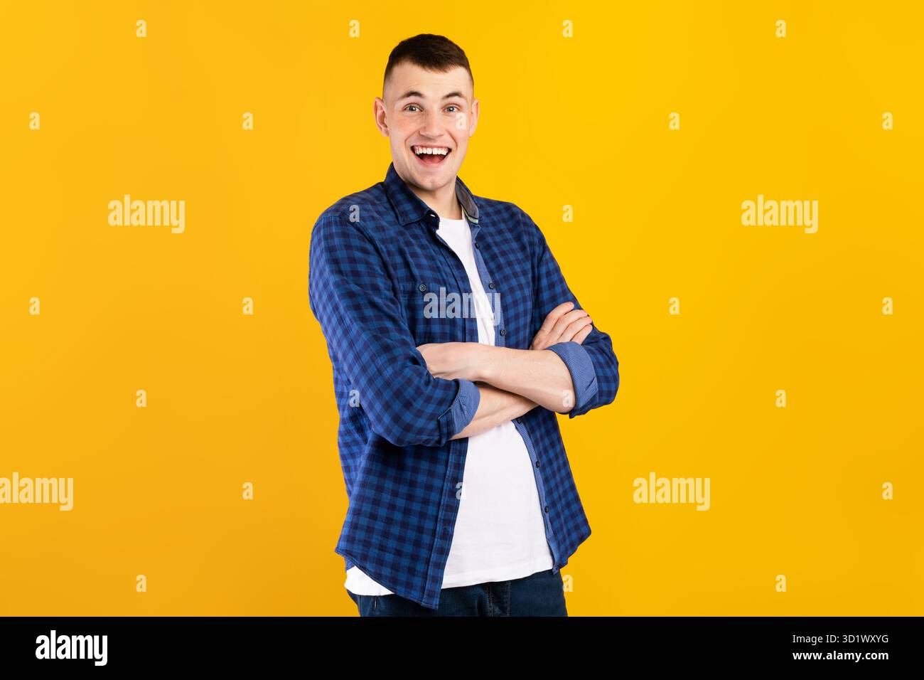 Allegro giovane uomo in piedi con le braccia incrociate davanti a uno sfondo giallo brillante Foto Stock