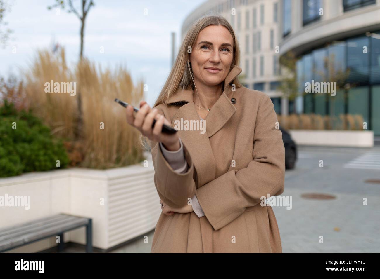Una donna d'affari si trova di fronte a un business center mentre guarda il telefono Foto Stock