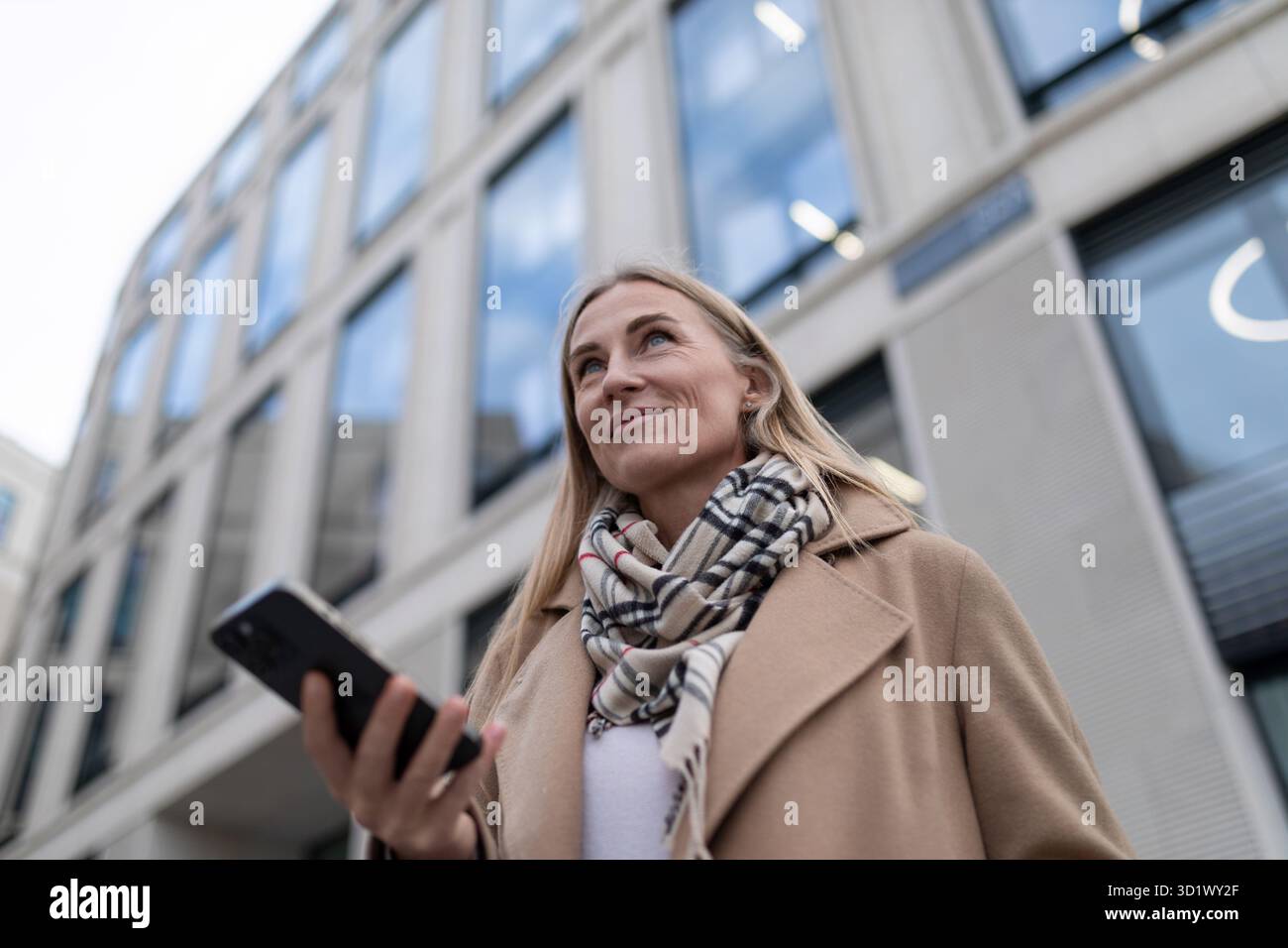 Una donna d'affari passa davanti a un moderno edificio di uffici mentre guarda il suo telefono Foto Stock