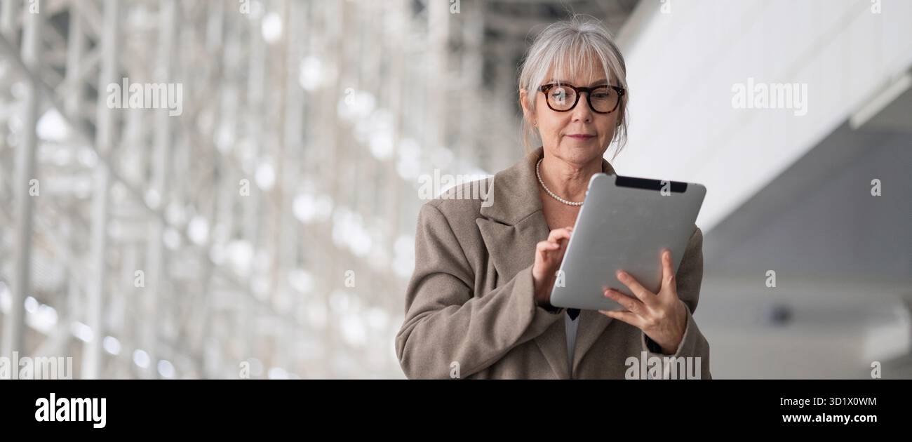 Donna d'affari di mezza età che usa un tablet mentre si trova in un ufficio moderno durante le ore diurne Foto Stock