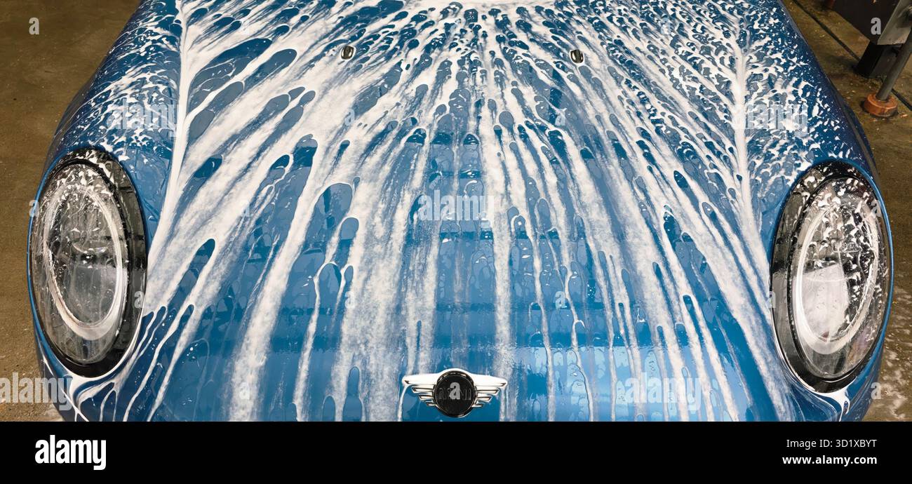 Berlino, Germania - 18 maggio 2025: Il cappuccio blu per auto è coperto di sapone durante il processo di lavaggio in garage. - Immagine stock catturata con smartphone