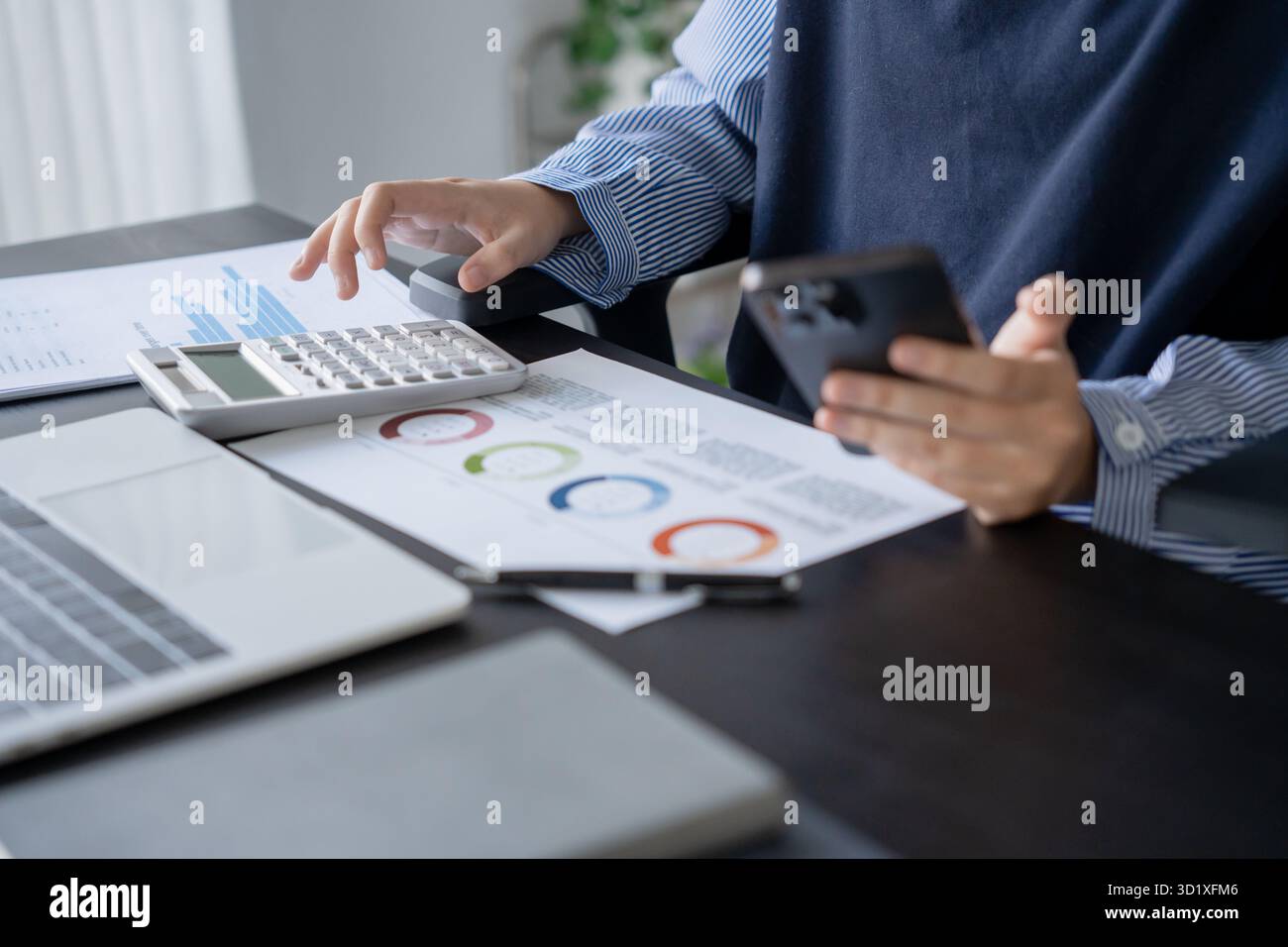 Donna d'affari asiatica che lavora con la calcolatrice e tiene in mano lo smartphone Foto Stock