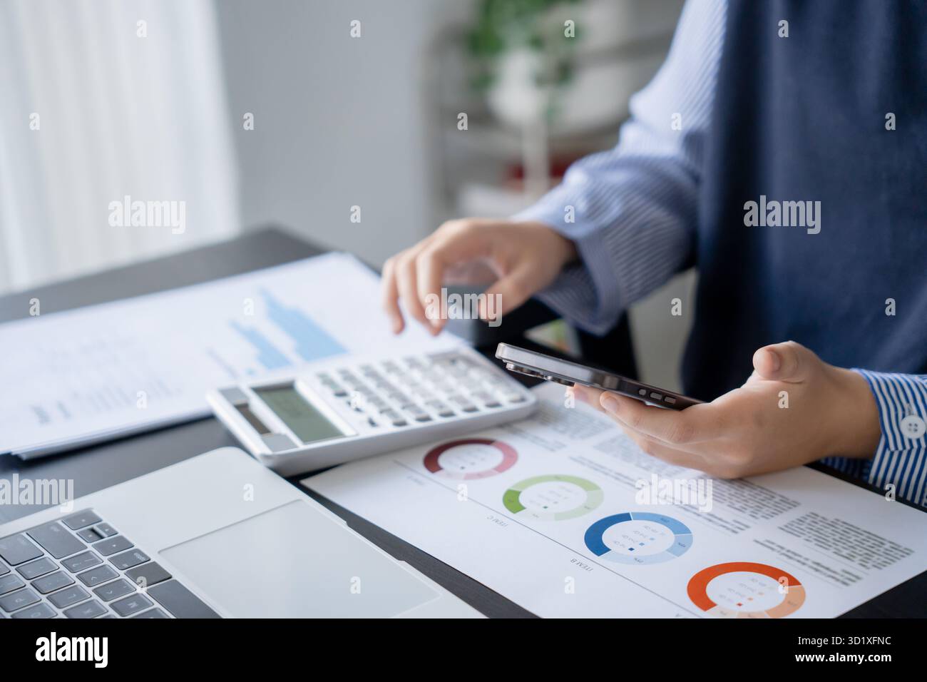 Donna d'affari asiatica che lavora con la calcolatrice e tiene in mano lo smartphone Foto Stock