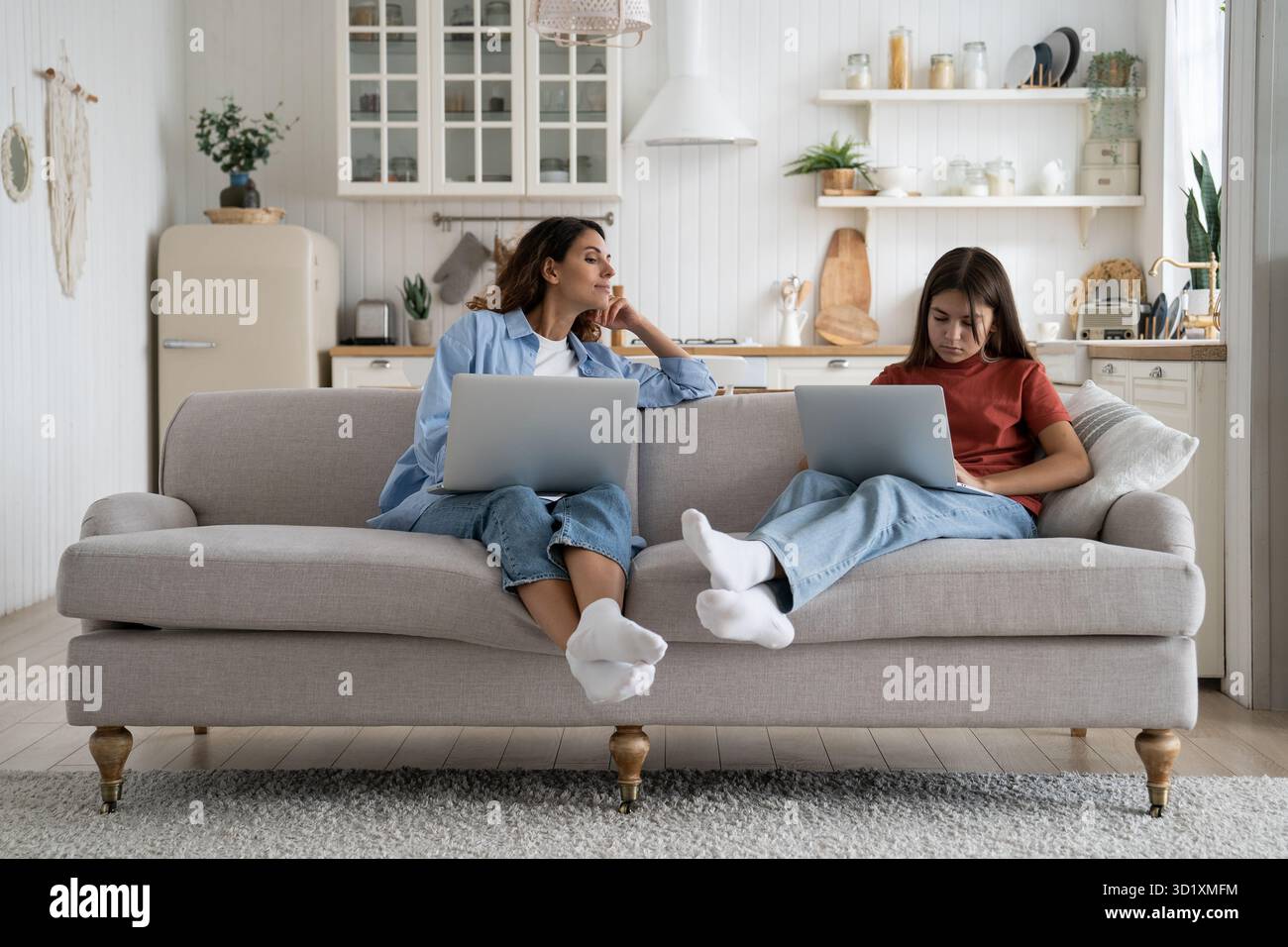 Famiglia madre e figlia utilizzano i notebook insieme mentre si siedono sul divano nel soggiorno di casa Foto Stock