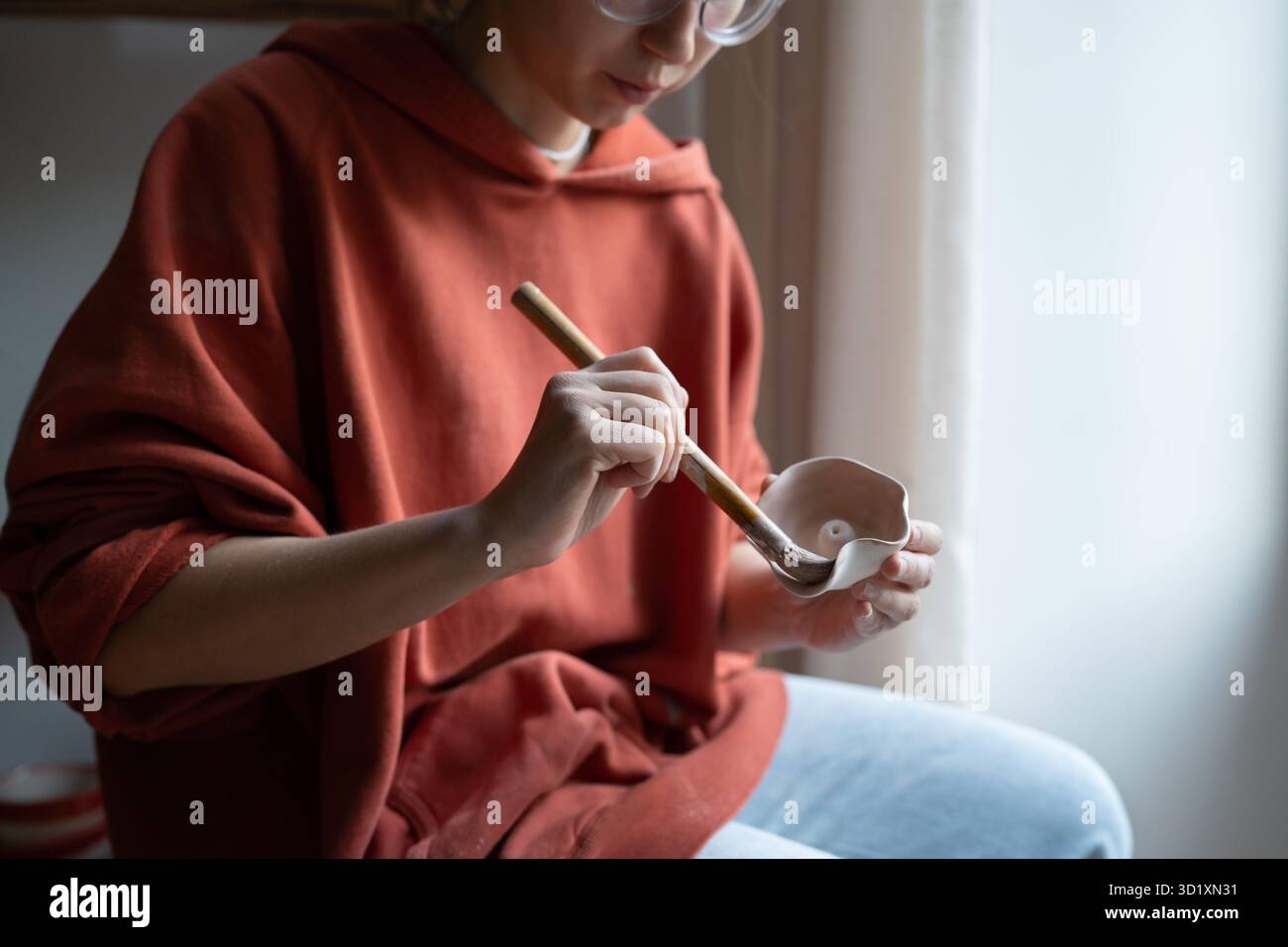Ragazza professionale seduta con pennello che applica vernice ai piatti in ceramica per proteggerli dai danni Foto Stock