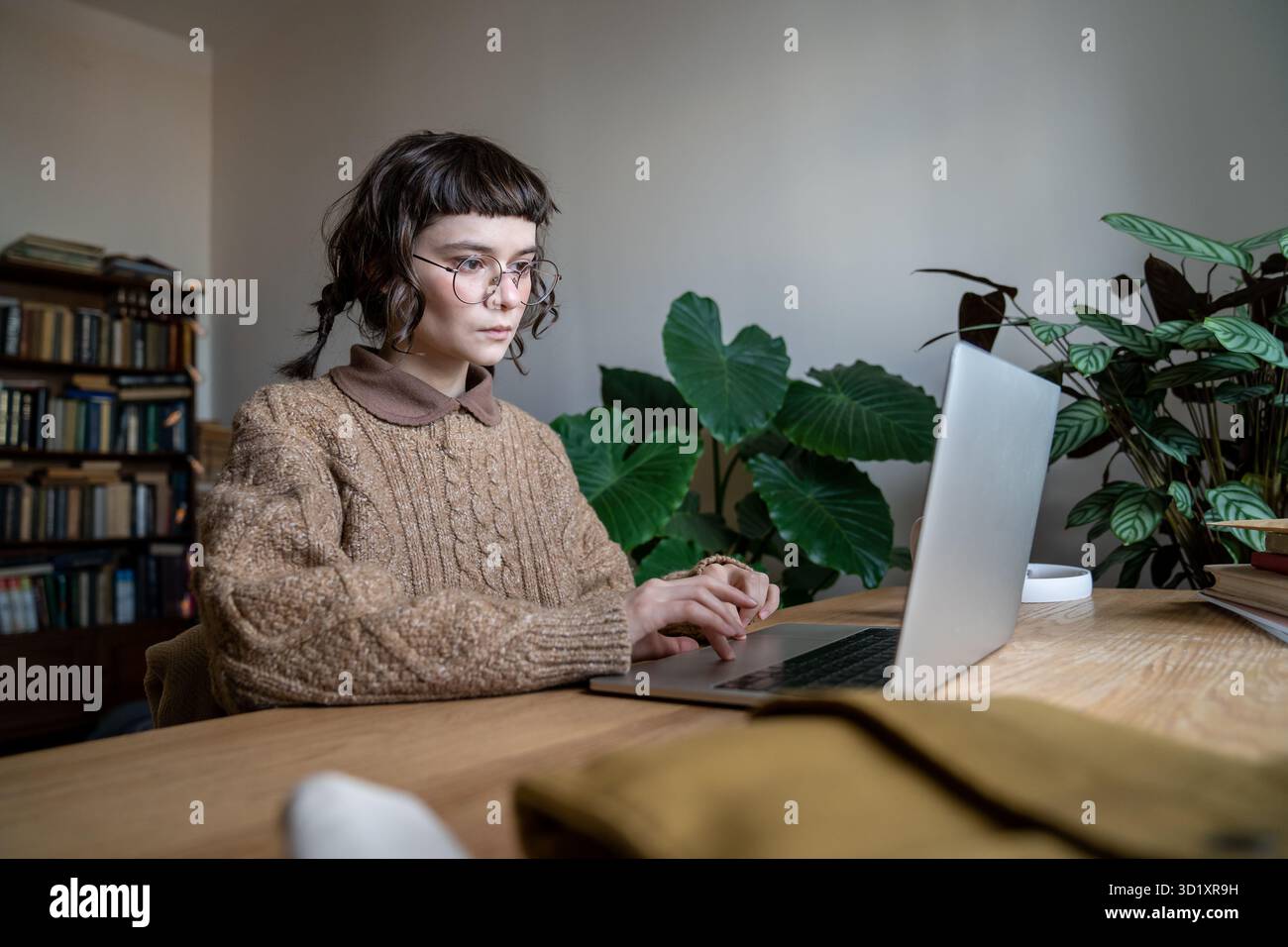Studentessa adolescente concentrata che indossa gli occhiali seduti al tavolo che digita sul laptop Foto Stock