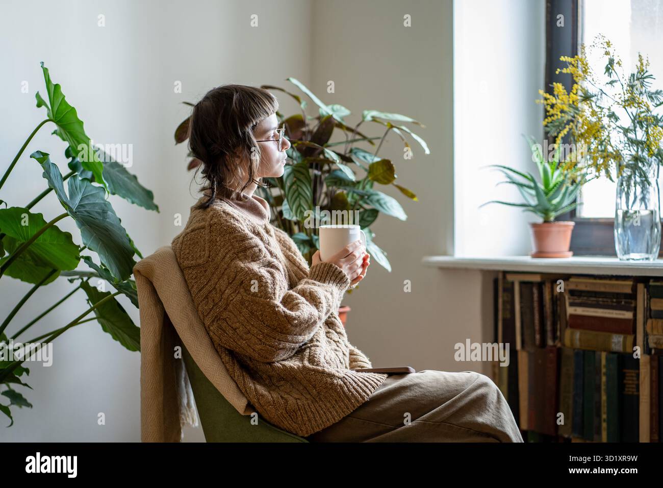 Una ragazza creativa e premurosa che sogna seduta sulla poltrona con una tazza di caffè guarda fuori dalla finestra e goditi il giorno Foto Stock