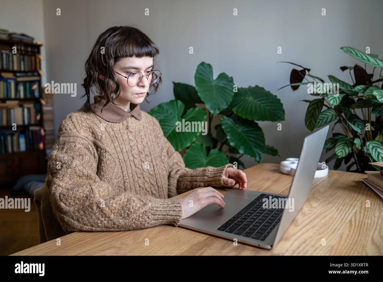 Studentessa adolescente concentrata che indossa gli occhiali seduti al tavolo che digita sul laptop Foto Stock