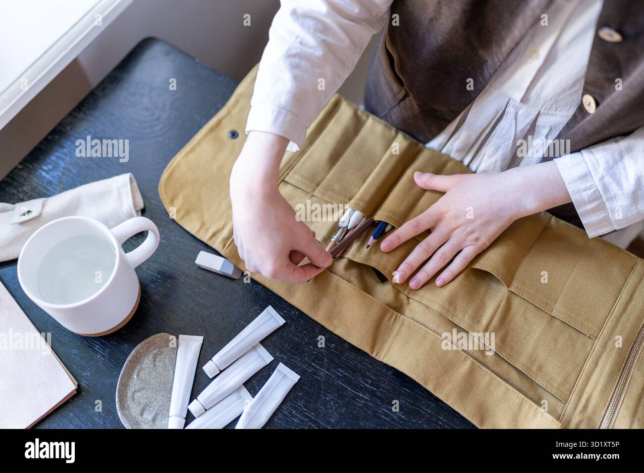 Astuccio pennelli da disegno appoggiato sul tavolo. Le mani femminili dell'artista raccolgono strumenti da disegno, matite, pastello. Foto Stock