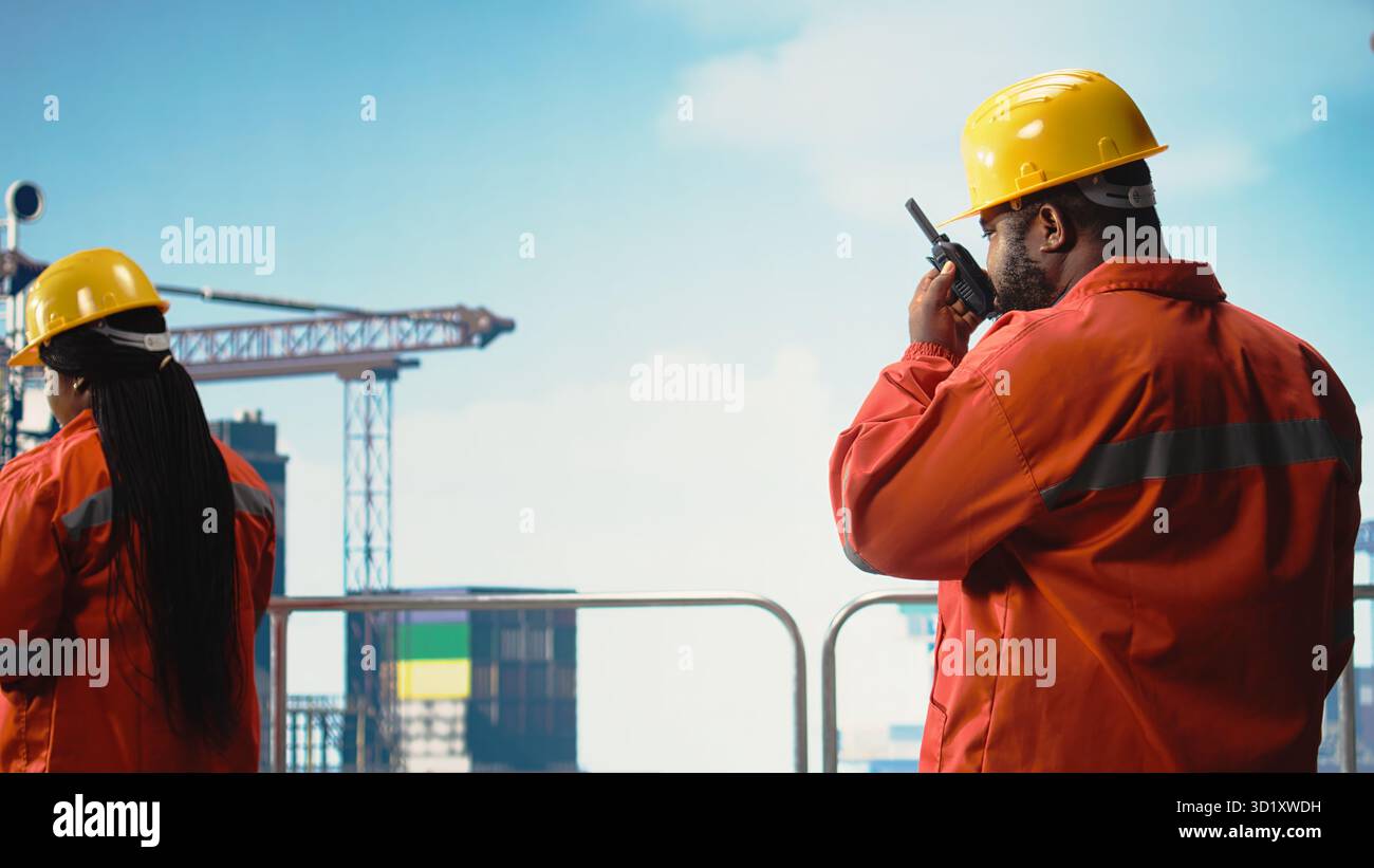 Operaio del carro di perforazione che utilizza un dispositivo radio portatile per monitorare i sistemi durante le operazioni. Uomo afro-americano sul ponte della piattaforma offshore che utilizza walkie talkie, apparecchiature di taratura, Foto Stock