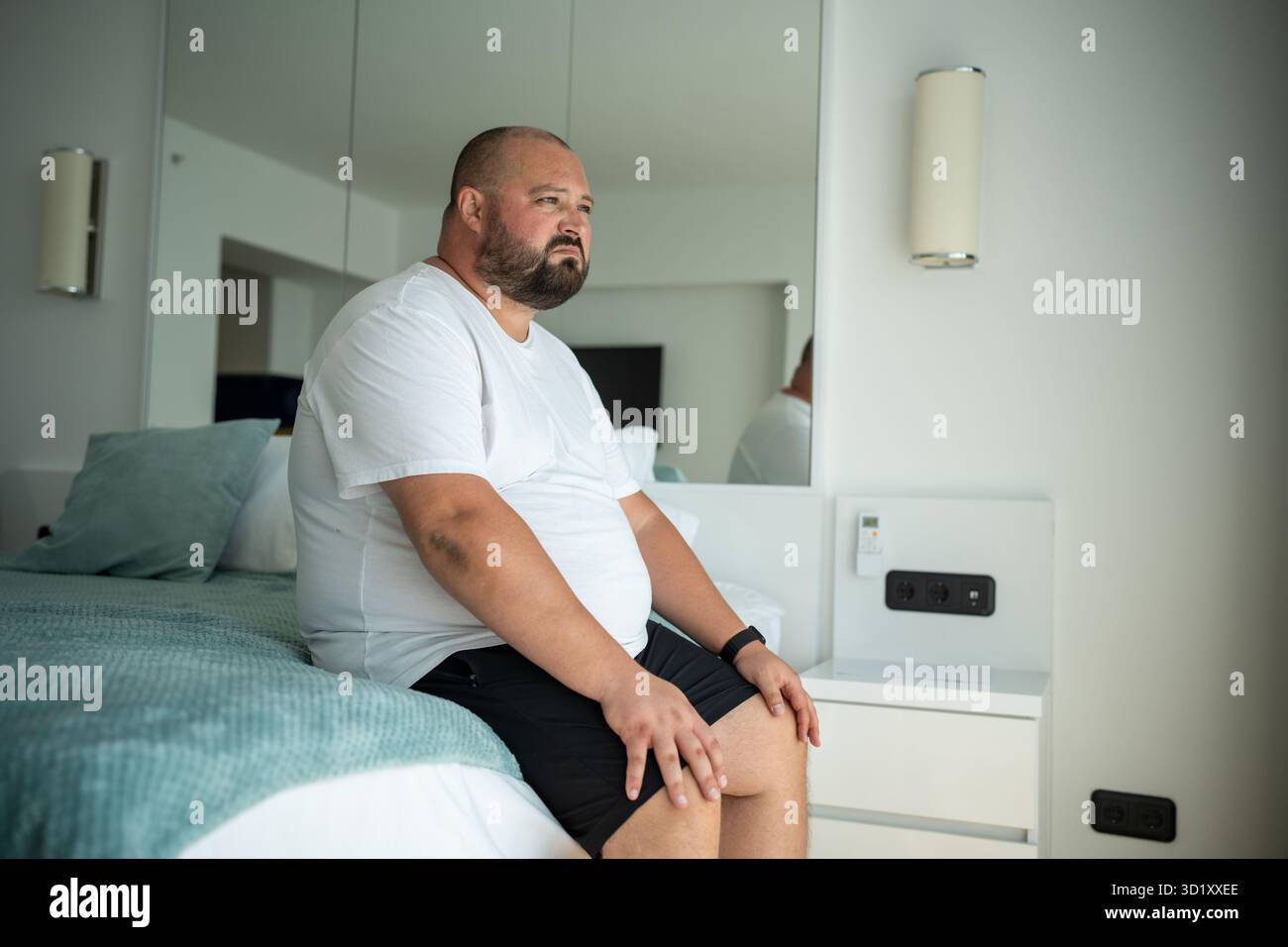 Un ragazzo grasso seduto sul letto con la faccia insoddisfatta. Il ragazzo si è svegliato dalla temperatura elevata di calore Foto Stock