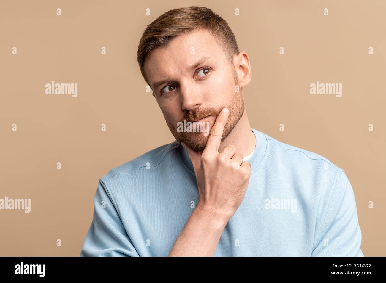Un uomo malvagio e premuroso che guarda verso l'alto il mento toccante su sfondo beige. Foto Stock
