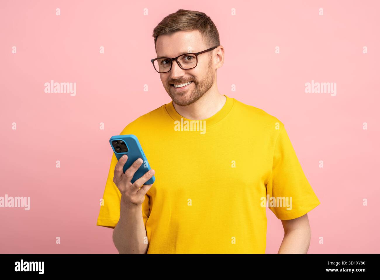 Soddisfatto delle buone notizie uomo barbuto sorridente in occhiali che guarda la fotocamera con il telefono cellulare in mano Foto Stock