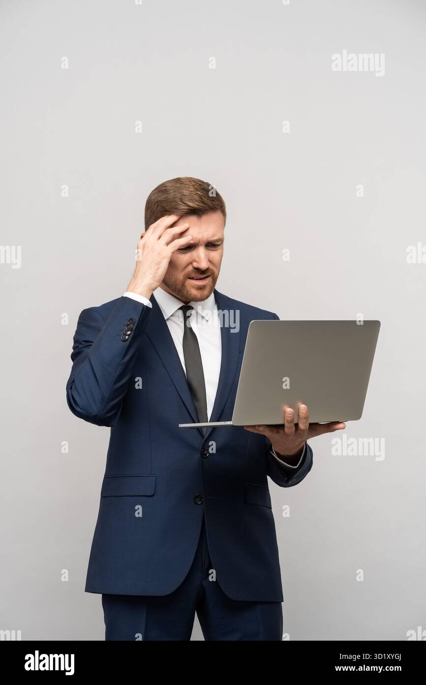 L'uomo ha problemi negli affari, scarsi risultati finanziari guardando il notebook su sfondo grigio. Foto Stock