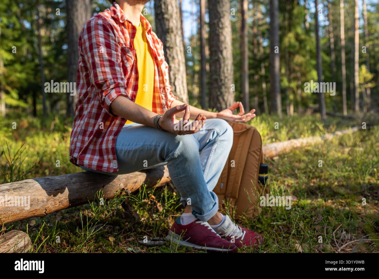 Uomo rilassato che riposa seduto sul tronco nella foresta meditando sulla natura facendo pratica spirituale. Foto Stock