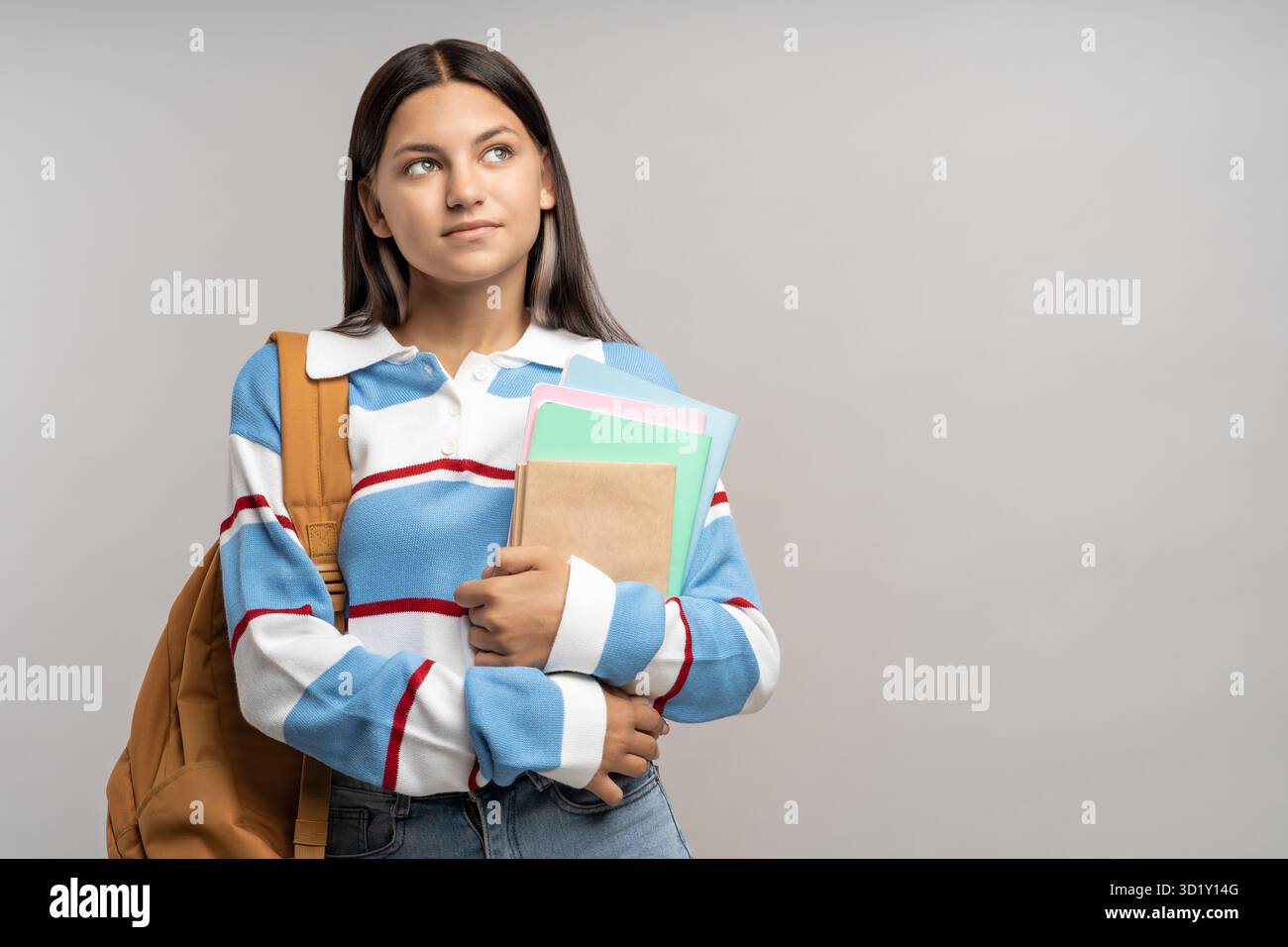 Interessata studentessa seria adolescente con zaino, copia libri su sfondo grigio. Foto Stock