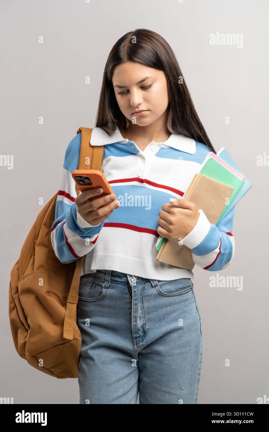 Annoiata e confusa studentessa che legge messaggi sul cellulare con confusa espressione del volto frustrata Foto Stock