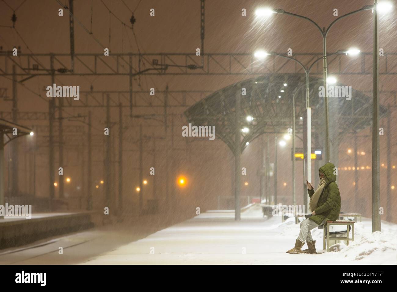 Giovane donna sulla piattaforma ferroviaria vuota in bufera in attesa di un treno. Maltempo Foto Stock