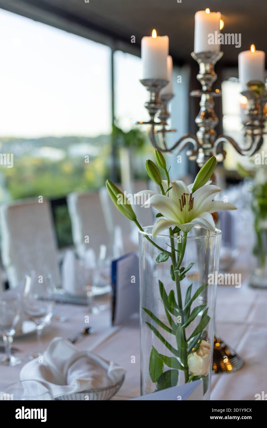 Un tavolo da pranzo splendidamente organizzato presenta alte candele bianche e un vaso di vetro con fiori freschi. L'ambiente è perfetto per una riunione serale, Foto Stock