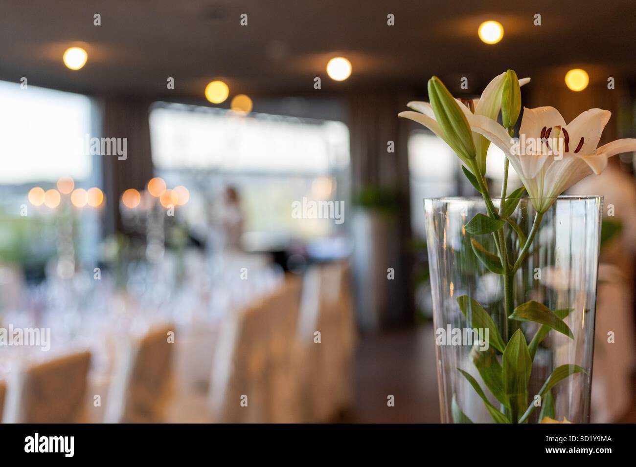Un'area da pranzo splendidamente arredata presenta un pezzo centrale floreale con gigli bianchi. L'illuminazione soffusa crea un'atmosfera calda, perfetta per le riunioni. G Foto Stock