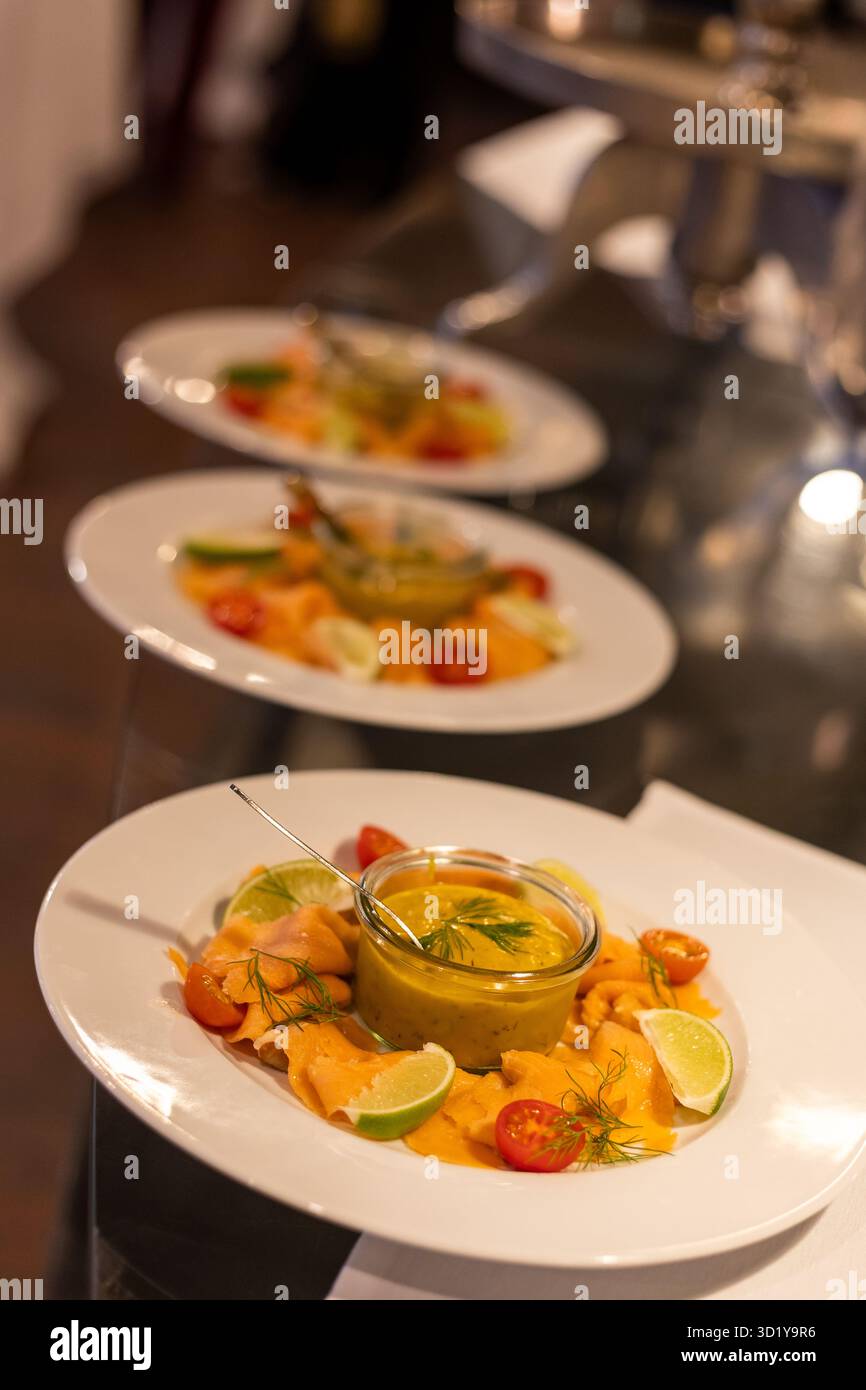 Tre eleganti piatti di salmone sono disposti ad arte su un tavolo durante un evento gourmet. Ogni piatto presenta decorazioni colorate e una salsa vivace, create Foto Stock
