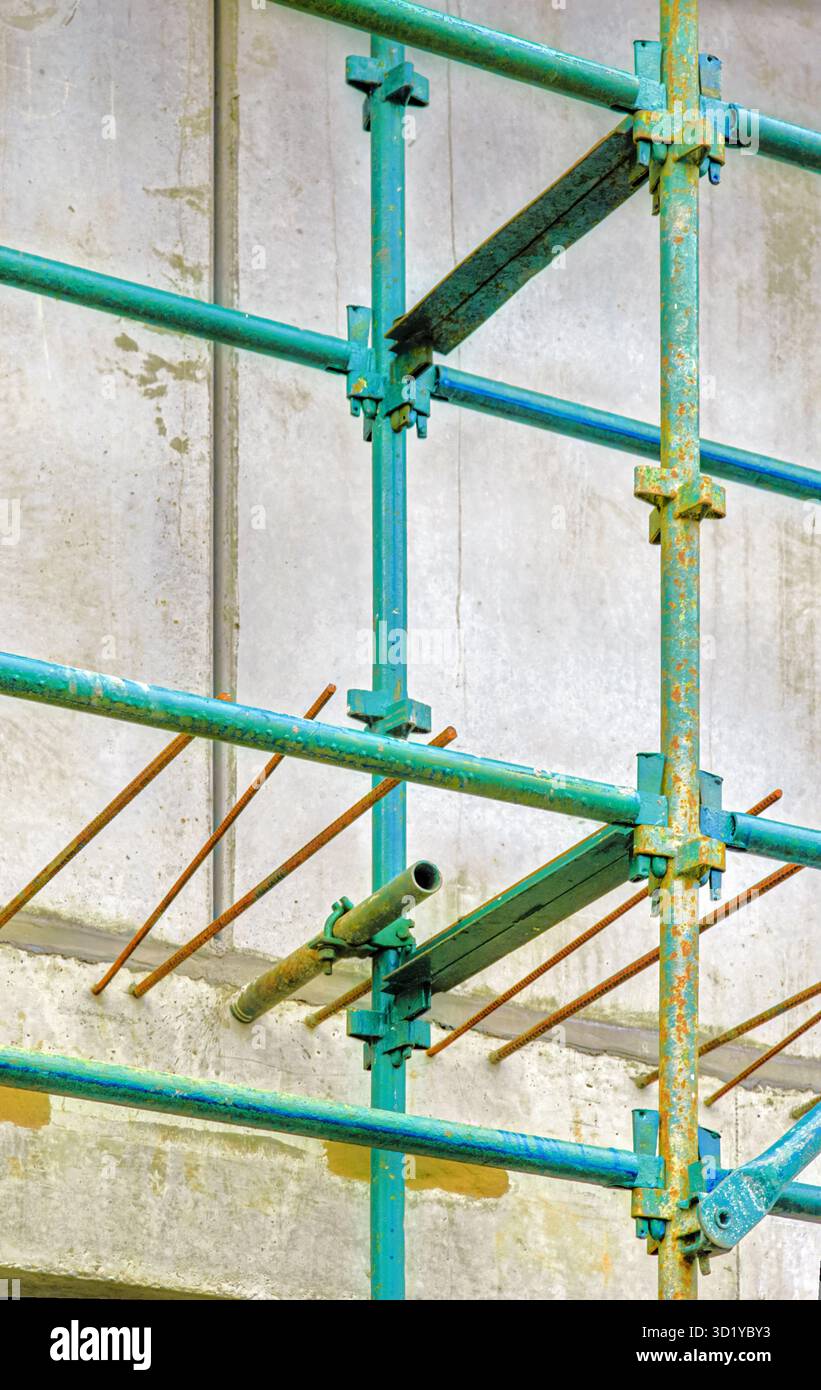 L'impalcatura verde circonda una fila di barre di rinforzo intemprate collegate a una semplice parete di cemento dietro Foto Stock