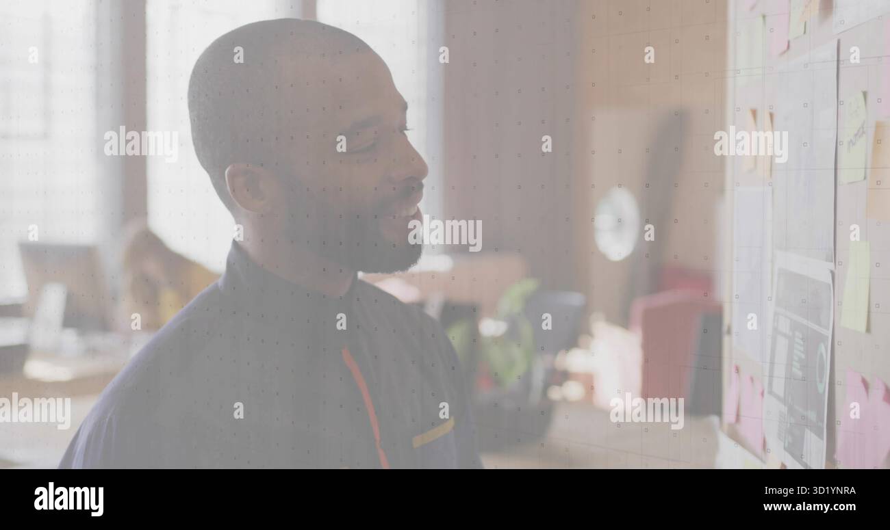 Uomo che indossa una camicia scura che rivede i piani al muro di mattoni in ufficio, con appunti e grafici adesivi Foto Stock
